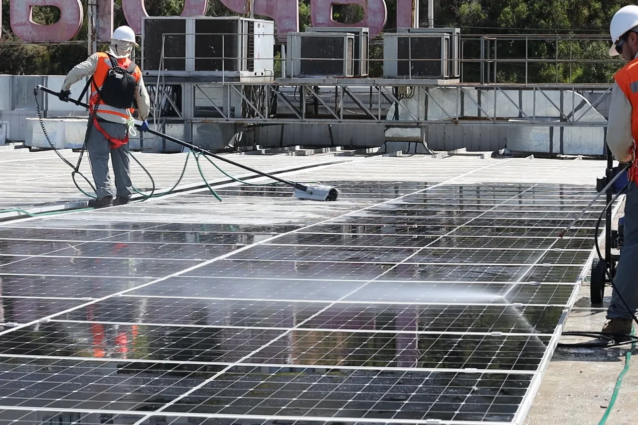 Dos operadores lavando módulos fotovoltaicos sobre la cubierta de un edificio.