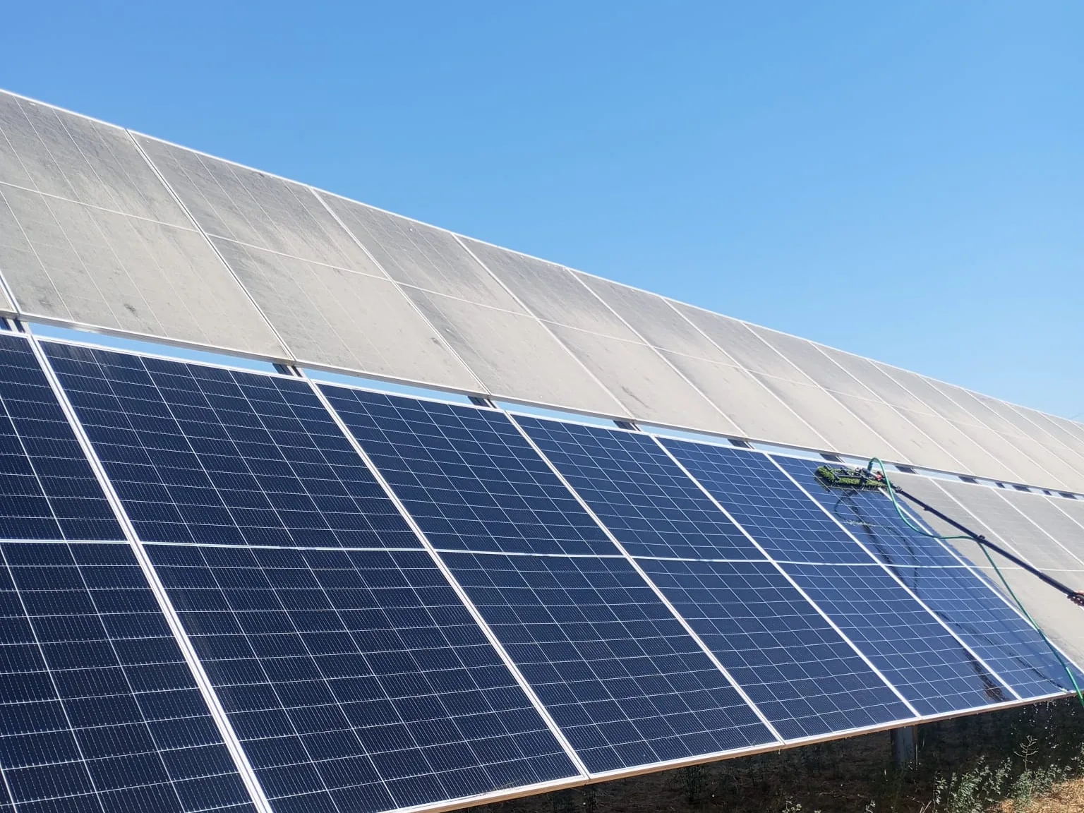 Hilera de paneles fotovoltaicos durante la limpieza: los módulos ya lavados contrastan con los que todavía tienen polvo acumulado.