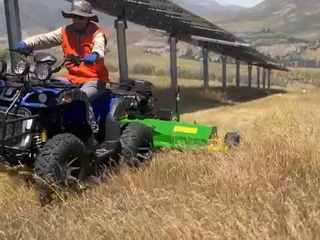 Operador de RAMAR Solar con cuadrimoto y desbrozadora controlando vegetación bajo las estructuras de una planta.